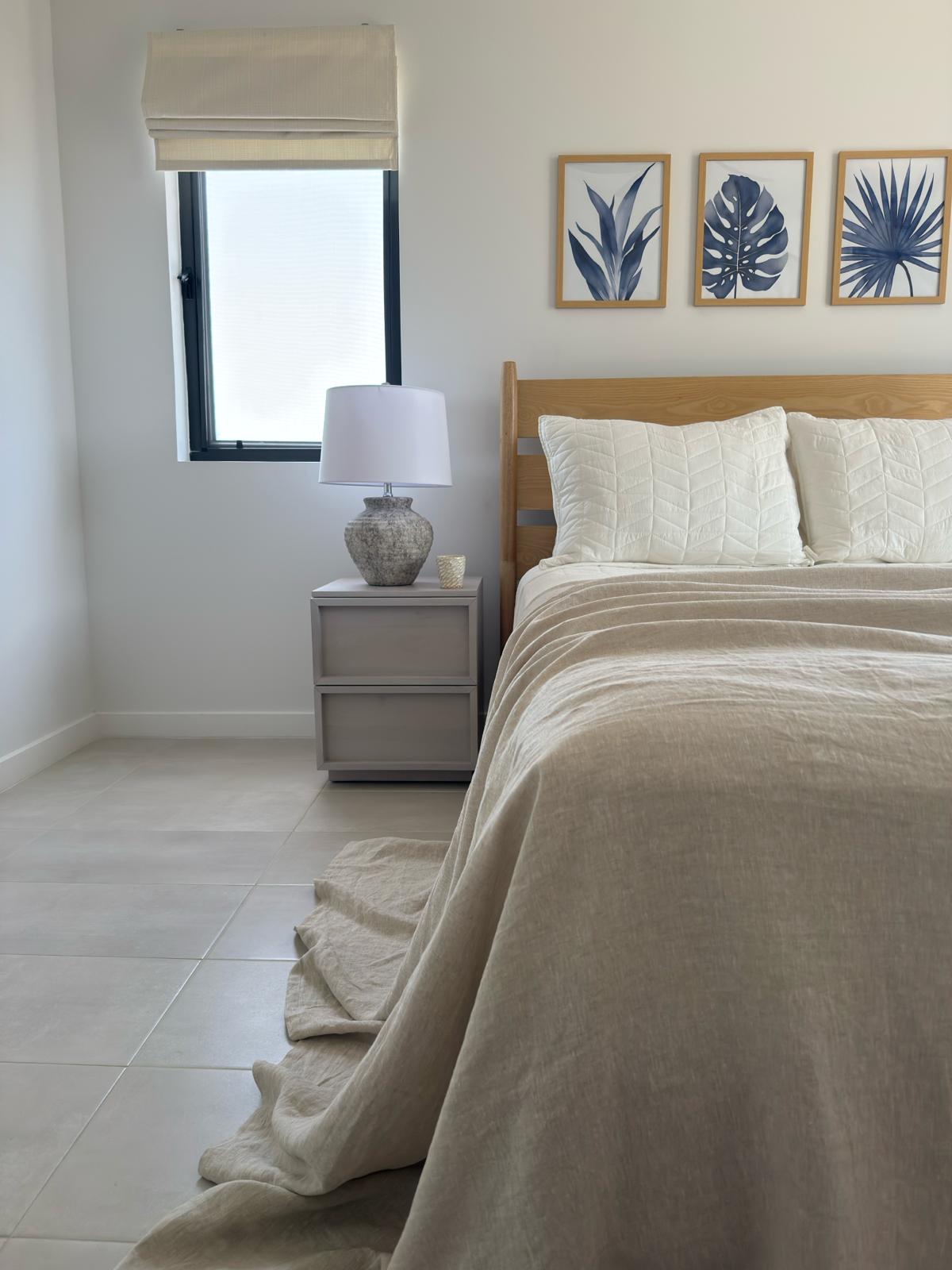 Modern apartment bedroom with neutral bedding and botanical artwork